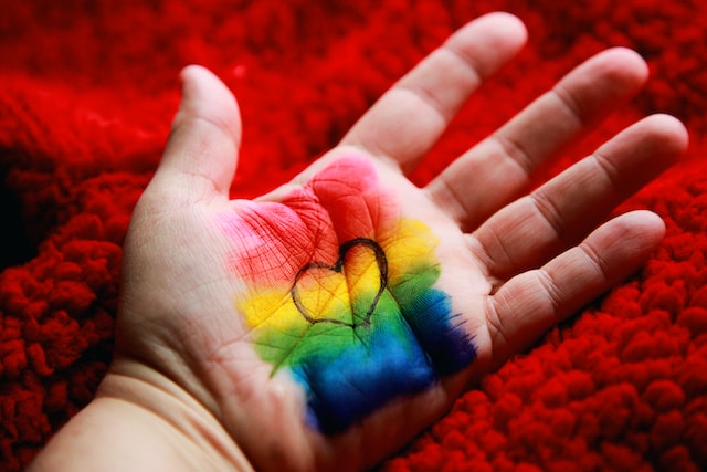  hand with rainbow paing and the black outline of a heart.