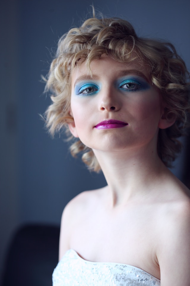 A youth drag queen with blue eye shadow and pink lipstick.