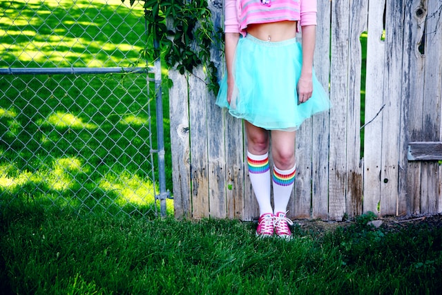 someone in a pink top, teal scirt and wite socks with rainbow stripes around the top.