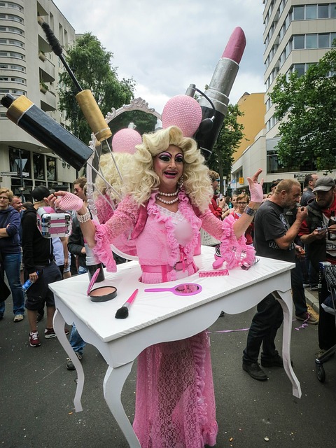 A drag queen wearing a big blond wig and a vibrant pink dress, standing in the middle of a table.