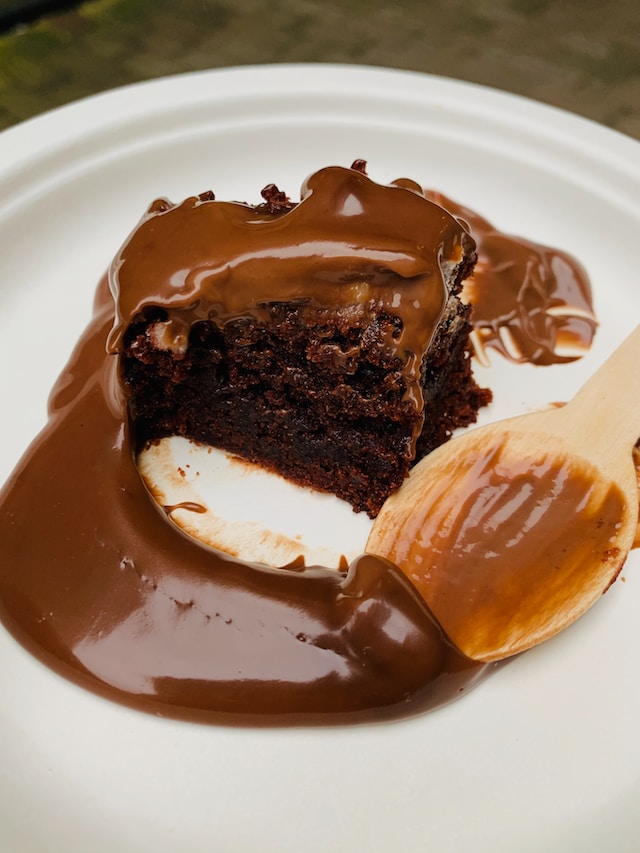 A bowl with a piece of brownie pudding and a spoon with pudding sauce on it.