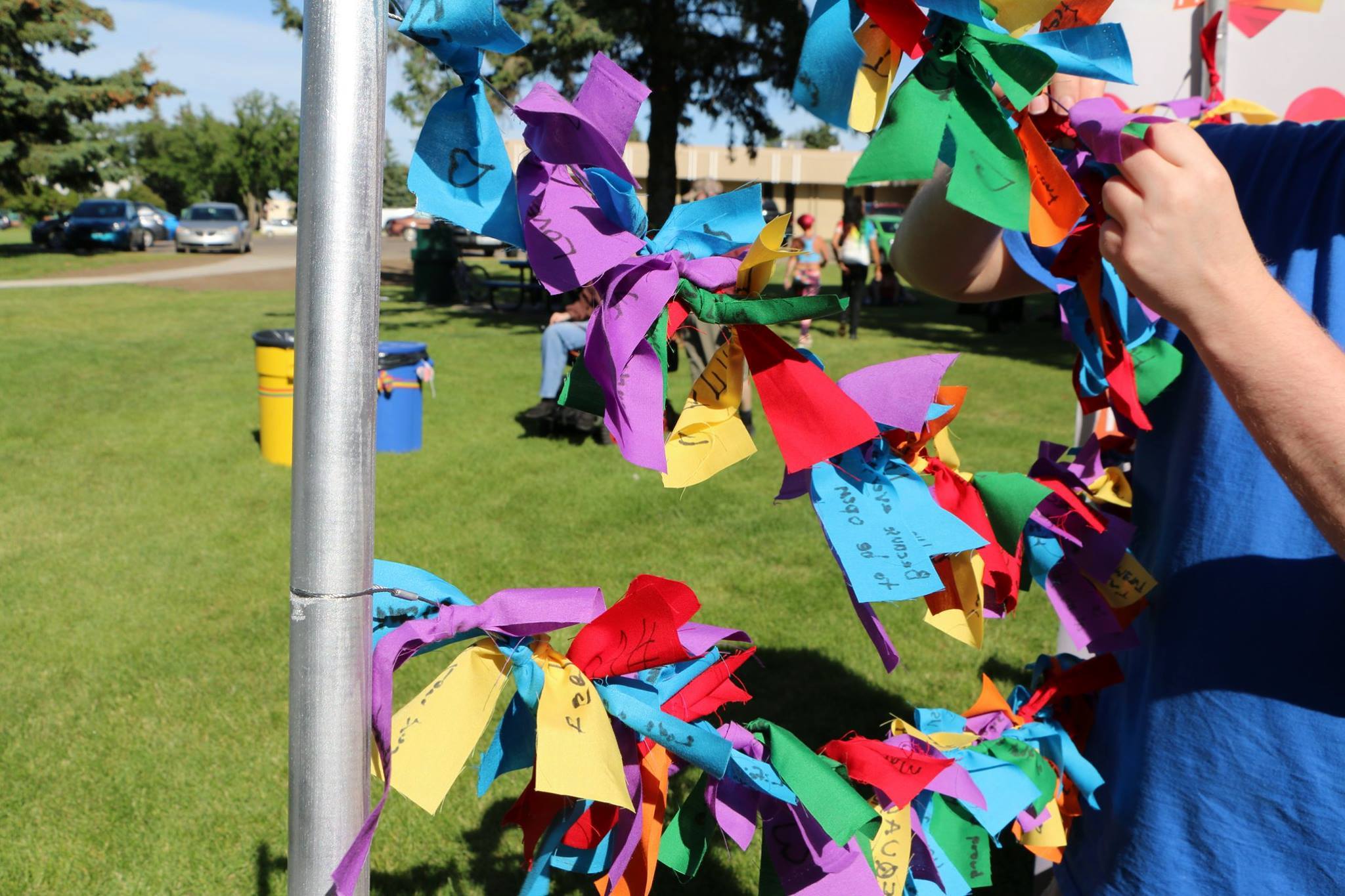 Wires with scraps of fabric tied to them. Each piece of fabric has a message written on them stating what Pride means to the individual who wrote the message.